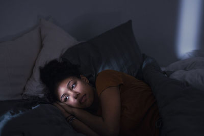 Pensive young woman lying in bed