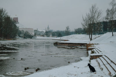 Scenic view of snow covered canal by buildings against sky