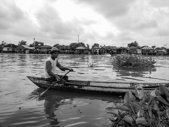 Man sitting on boat in river against sky