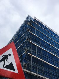 Low angle view of road sign by building against sky