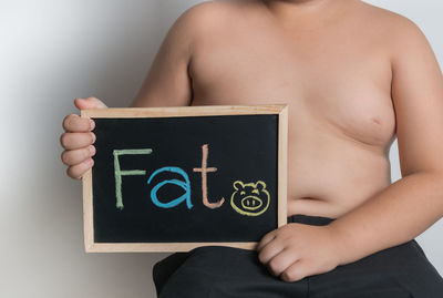 Midsection of shirtless man holding text on blackboard