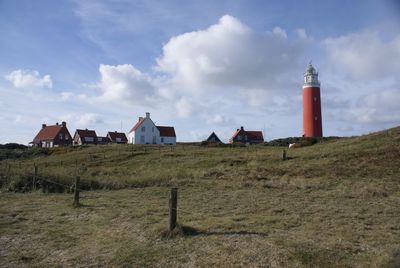 Lighthouse on field by buildings against sky