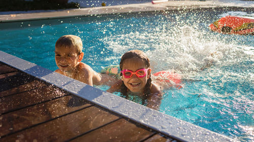 Kids play in swimming pool at sunny day, refresh at heat weather, active summer vacation
