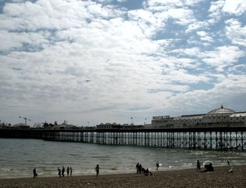 People on pier by sea against sky in city
