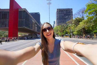 Low angle view of young woman wearing sunglasses against buildings