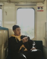 Rear view of man seated in the train looking through the window 