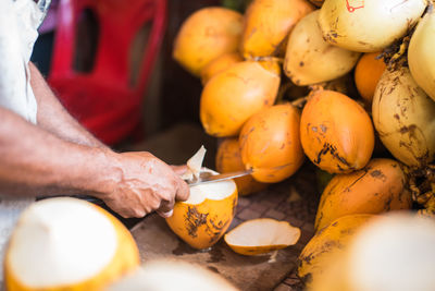 Cropped hands on vendor peeling coconuts at market stall