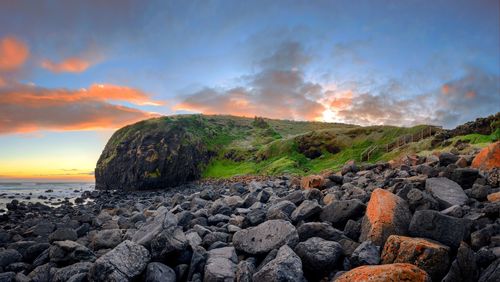 Rocks on beach against sky during sunset