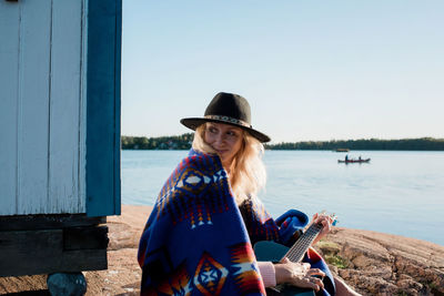 Portrait of a woman sat playing a guitar by the water in the sun