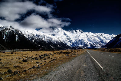 Road leading towards snowcapped mountains against sky