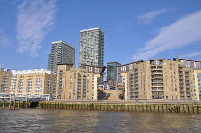 Modern buildings by river against blue sky