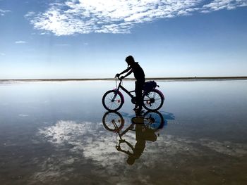 Man riding bicycle by sea against sky