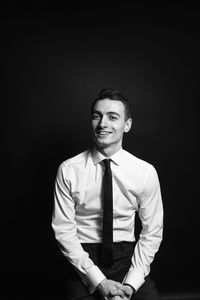 Portrait of smiling businessman sitting against black background