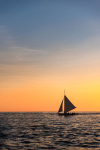 Sailboat sailing on sea against sky during sunset