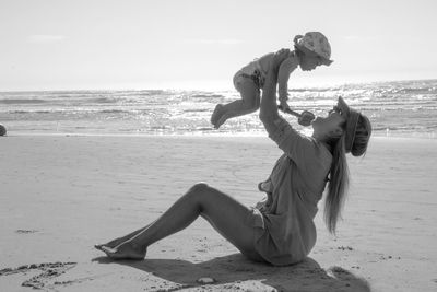 Full length of happy mother with arms raised holding baby at beach during sunny day