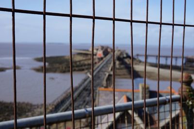 Metal fence by sea against sky