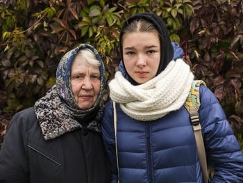 Portrait of granddaughter and grandmother standing against plants during winter