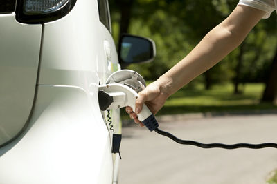 Cropped hand of person charging white electric car