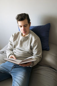 Portrait of young woman reading book while sitting on sofa at home