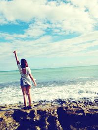 Rear view of woman standing at beach against sky