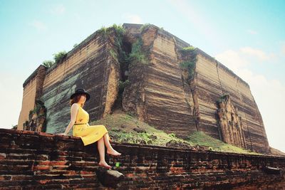 Young woman looking away while sitting against built structure