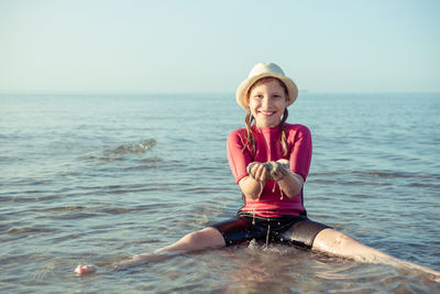 Portrait of smiling girl sitting on sea against sky