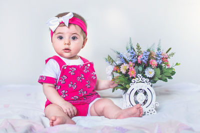 Portrait of cute baby girl with flowers sitting on bed at home