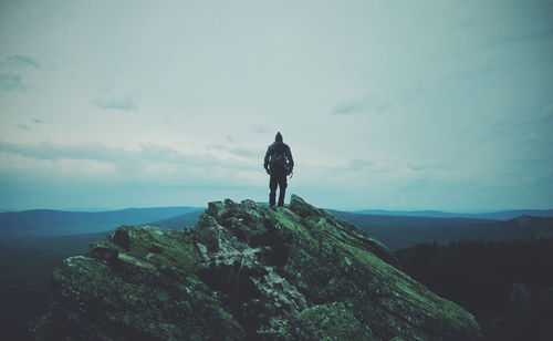 Rear view of man standing on rock against sky