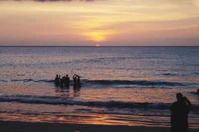 Silhouette people on beach against sky during sunset