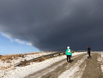Rear view of people walking on road against sky during winter