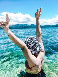Woman with arms raised standing in sea during sunny day