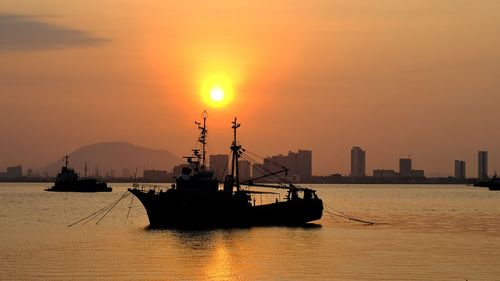 Silhouette sailboats in sea against orange sky