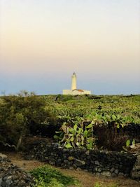 Lighthouse on field by building against sky