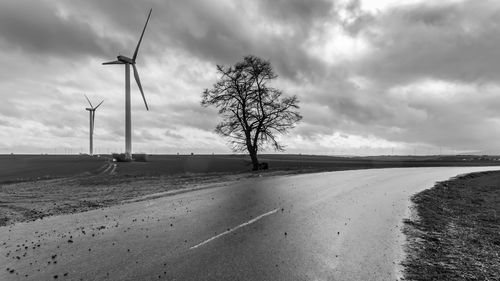 Windmill on road by land against sky