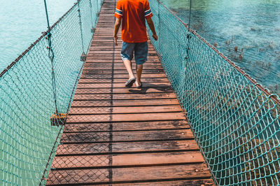 Rear view of a boy walking on a suspended footbridge