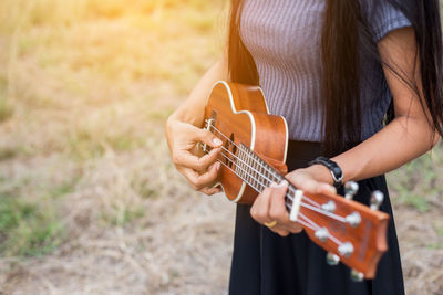 Midsection of woman playing guitar on field