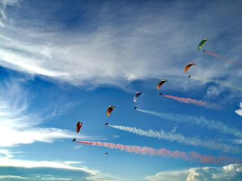 Low angle view of powered parachutes with colorful vapor trails against sky during airshow