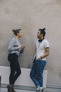 Male and female computer programmers discussing while leaning on wall in office