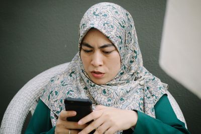 Woman in hijab using mobile phone against wall