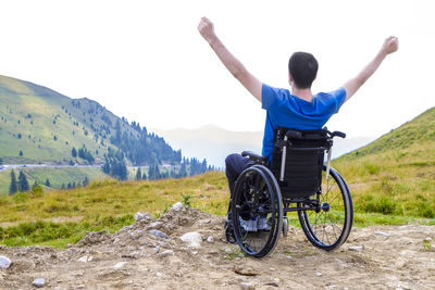 Rear view of man with arms outstretched sitting on wheelchair at landscape