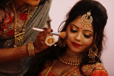 Beautician applying make-up on bride face during wedding