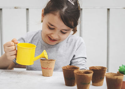 Little happy caucasian girl  holds a yellow watering can  and waters cardboard glasses