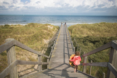 Rear view of women on railing by sea against sky