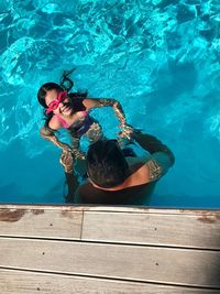 High angle view of father assisting daughter in swimming pool