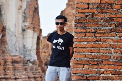 Young man wearing sunglasses standing against brick wall