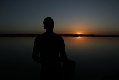 Silhouette man standing by lake against sky during sunset