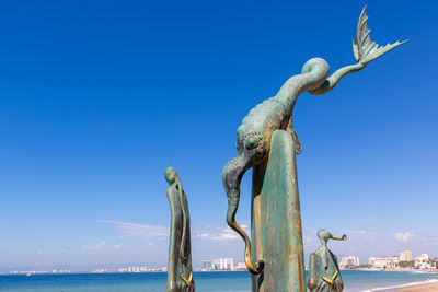 Statue by sea against clear blue sky