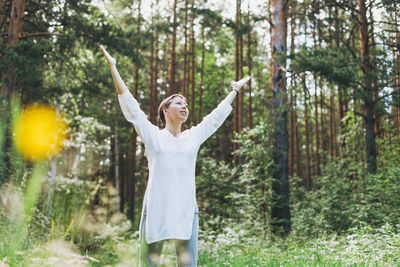 Woman with arms raised standing amidst trees