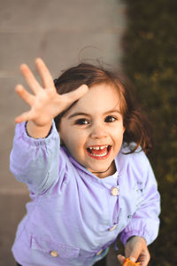 High angle portrait of cute smiling girl with hand raised standing in park
