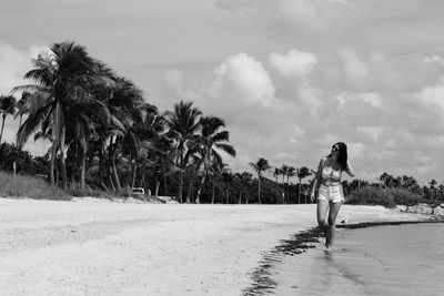 Young woman walking on shore at beach against cloudy sky